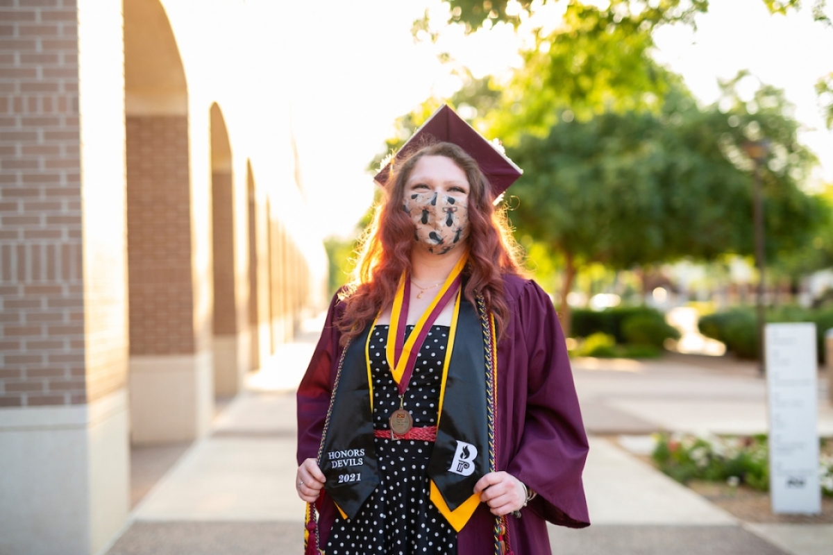 woman wearing a mask and a cap and gown standing outside of a building