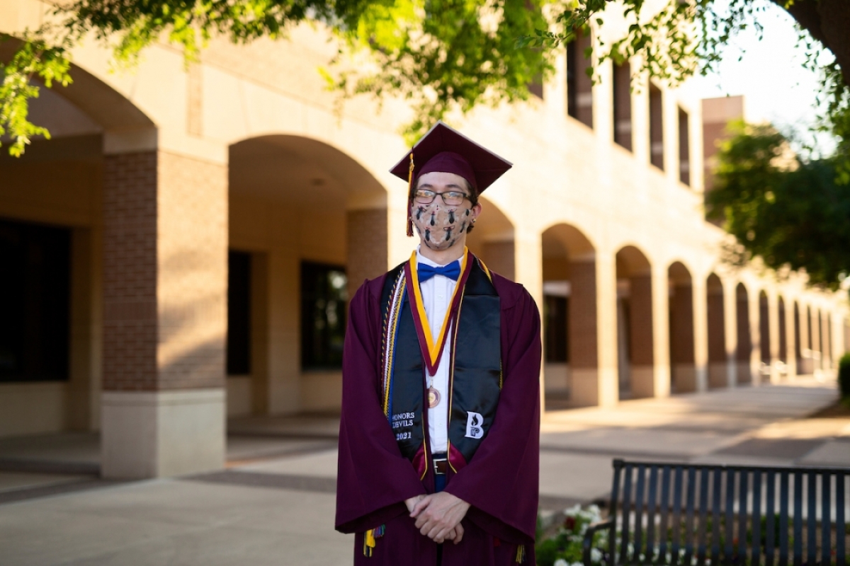 man wearing a mask and a cap and gown standing outside of a building