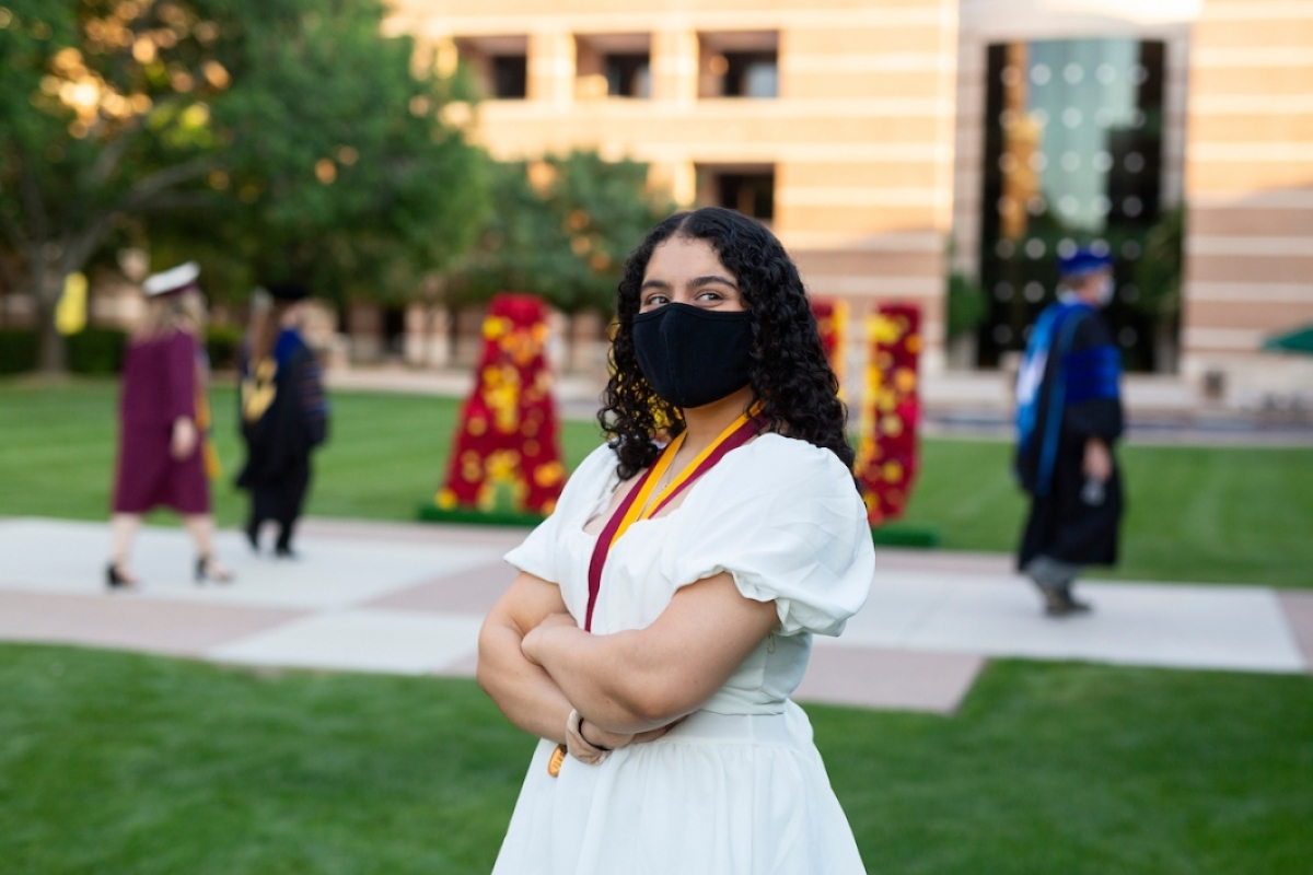 woman in a mask and white dress poses on ASU West campus' Fletcher Lawn
