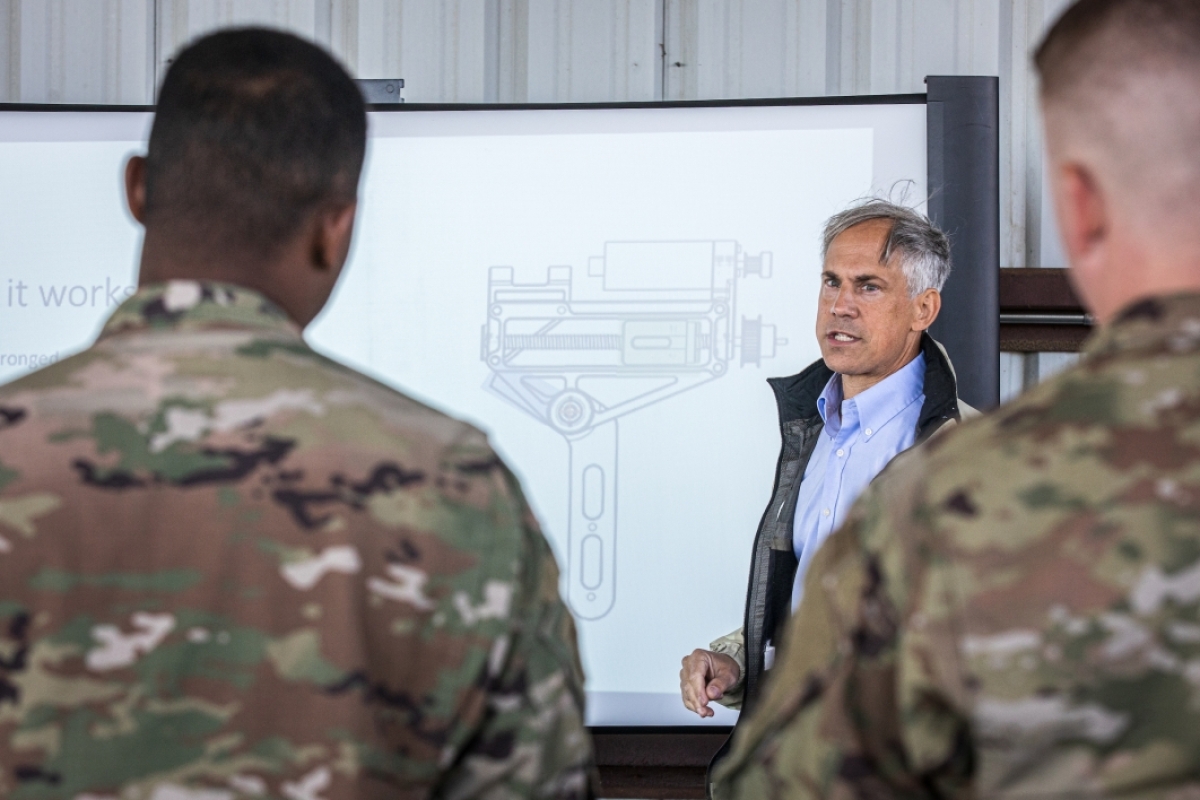 A man not in uniform explains a diagram on a board to a group of military members