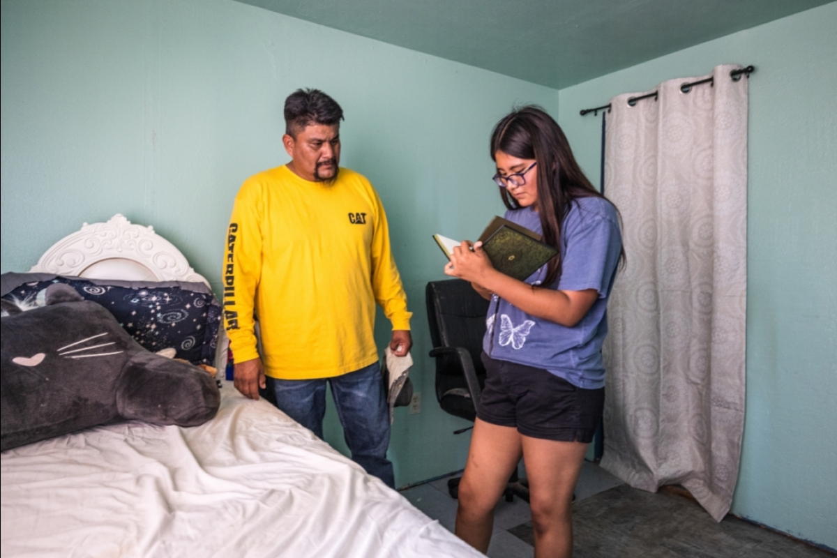 A father speaks to his teen daughter in her sparsely decorated bedroom