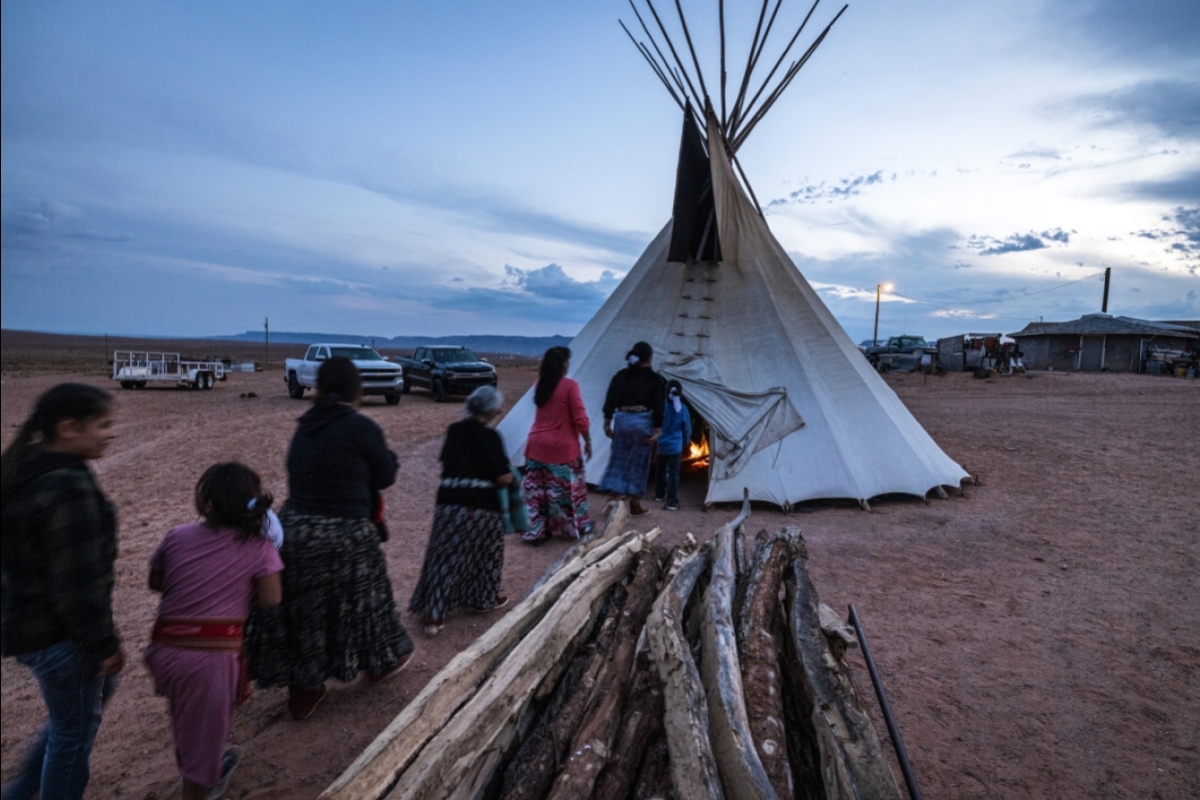 A line of family members walks into a teepee at sunset