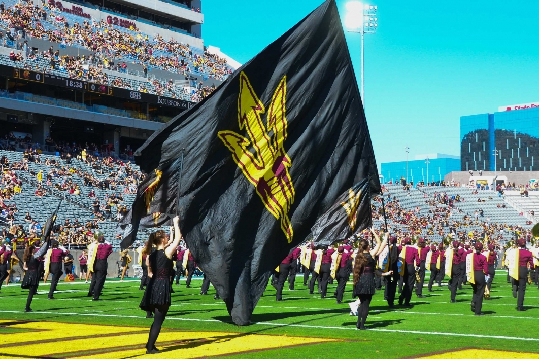 The ASU Marching Band on the football field with a giant black pitchfork flag