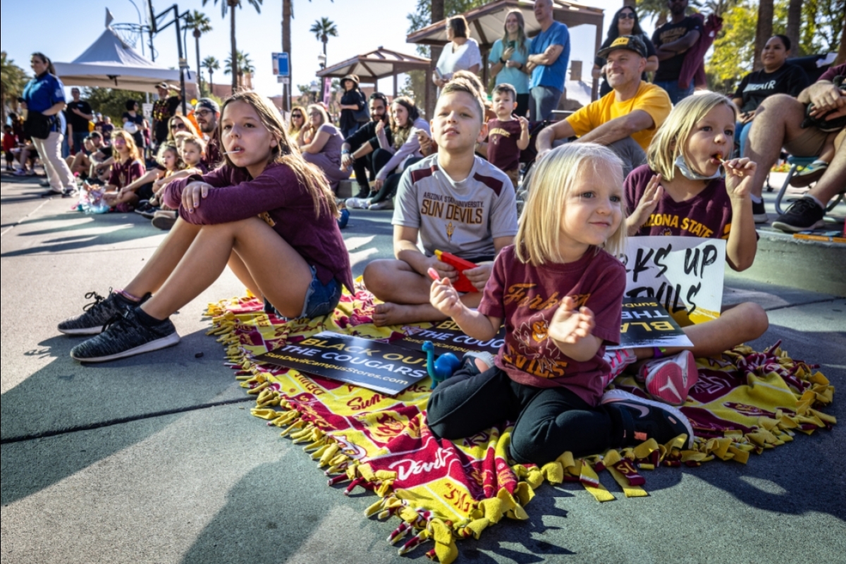 Four young siblings sit on an ASU blanket to watch the Homecoming parade