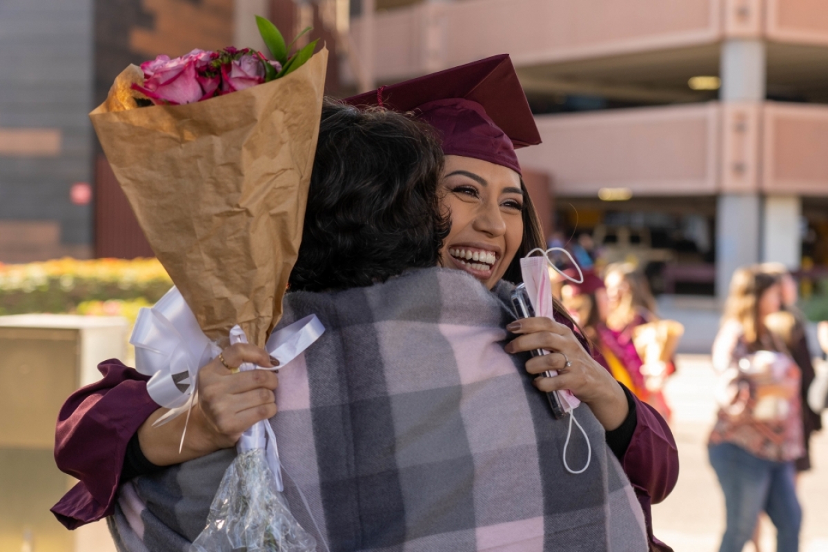 student holding flowers and hugging mom after graduation