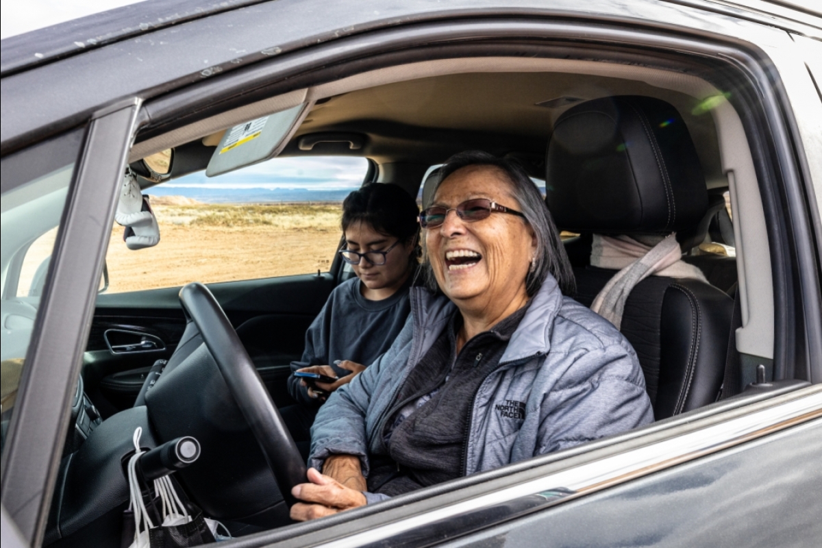 A Navajo grandma laughs behind the wheel of an SVU with her granddaughter next to her