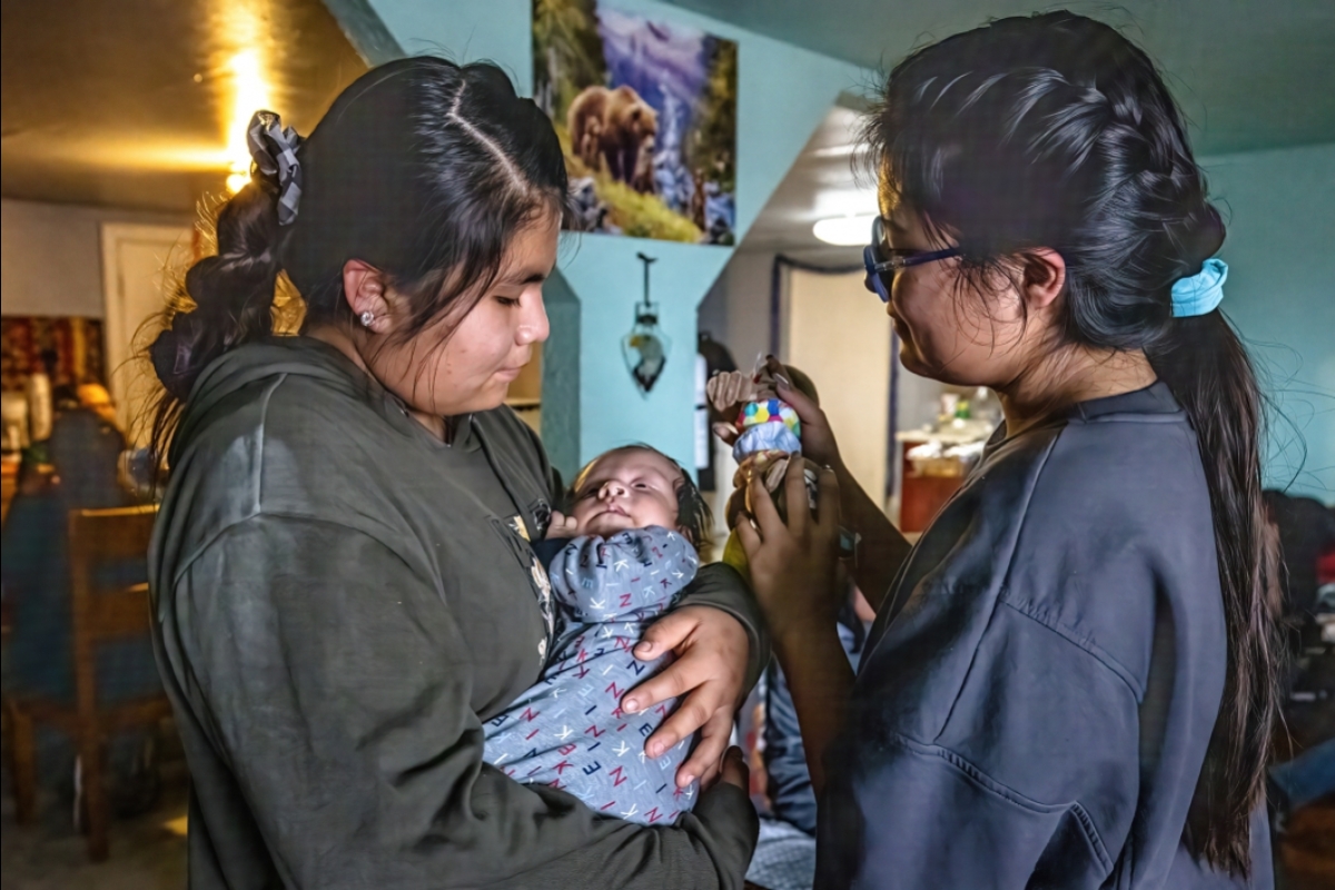 A young Navajo woman holds her baby cousin as her sister looks on