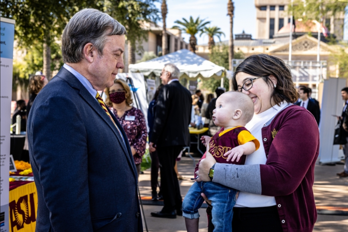 Woman holding baby as ASU President looks on