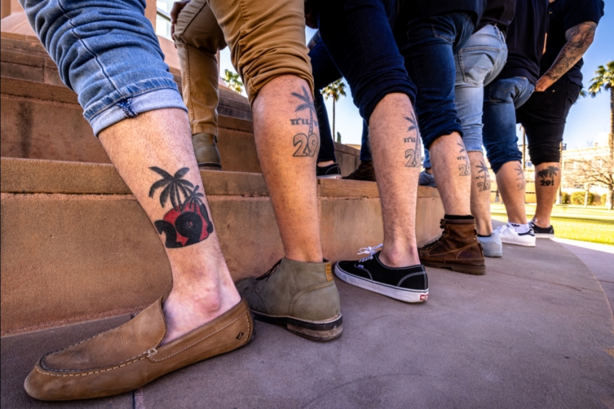 The back of the calves of seven men, showing a tattoo of a palm tree and the number 29.