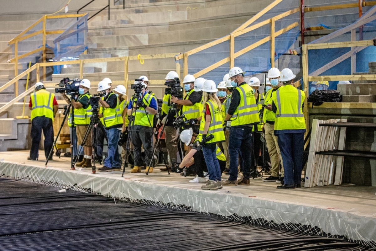 Members of the media wearing hard hats and yellow vests film the floor of the new ASU arena