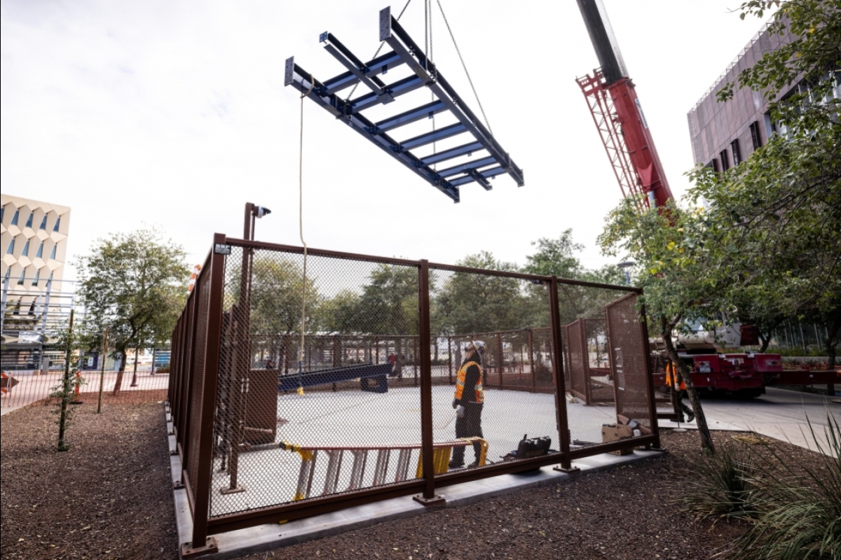 A crane moves a large piece of metal into a fenced area