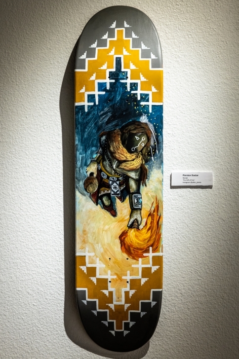 Skateboard painted with an image of a person lighting a fire, surrounding by abstract shapes.