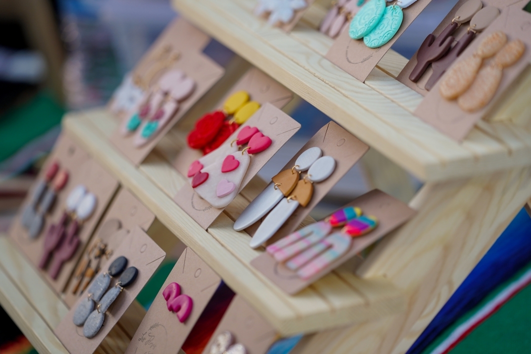 Wooden display case holding several pairs of colorful clay earrings.