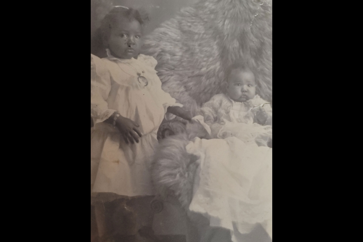 Old black-and-white photo of young African American girl and baby.