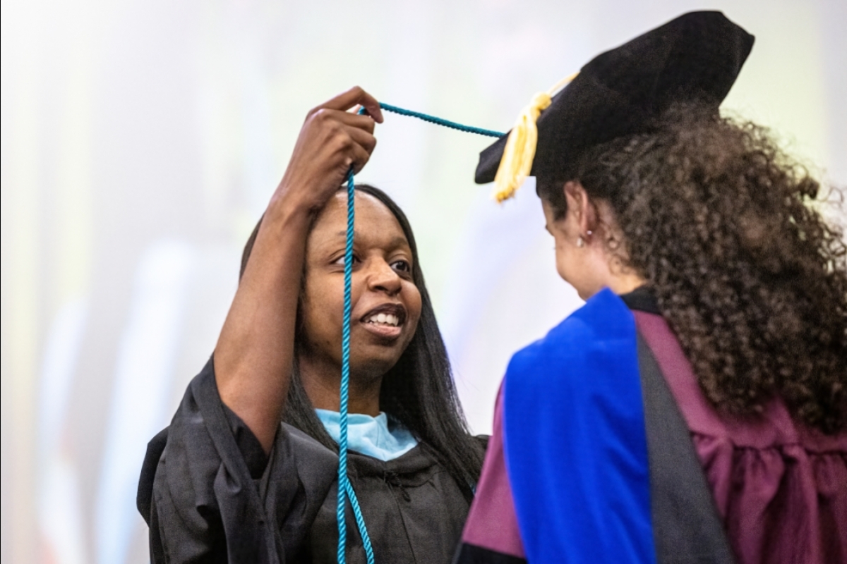 A woman in graduation regalia slips an honor cord over a student's head