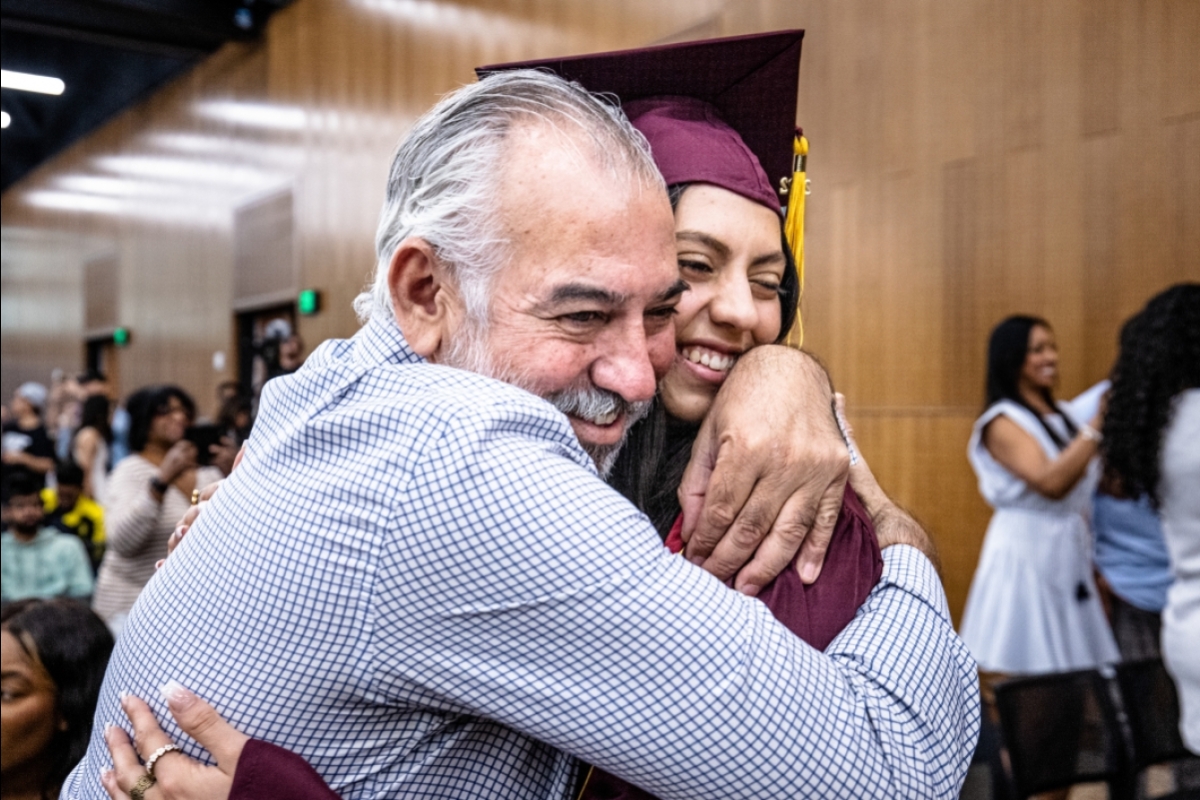 A father gives a big hug to his college graduate daughter in cap and gown