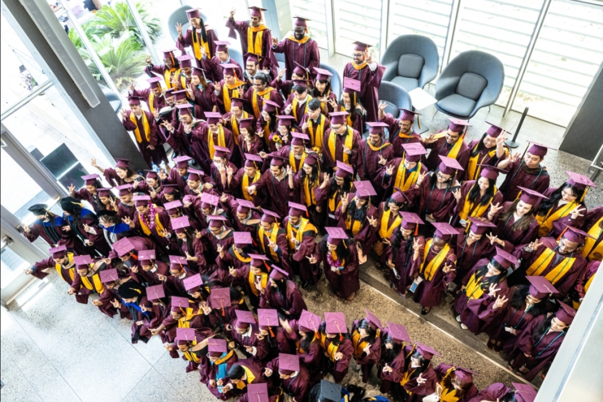 An overhead photo of scores of people in cap and gown posing for a group photo