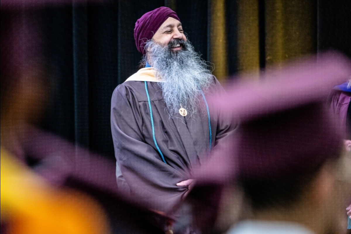 A man with a very long beard smiles as he watches students enter a convocation ceremony