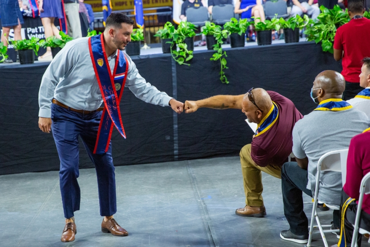 A man walking down an aisle at a veterans stole ceremony gets a fist bump from a man sitting in the audience