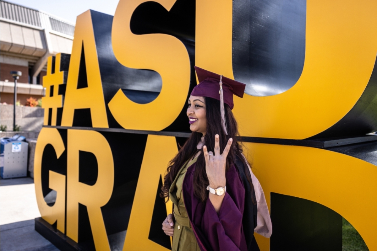 ASU student posing in front of large ASU Grad sign in cap and gown