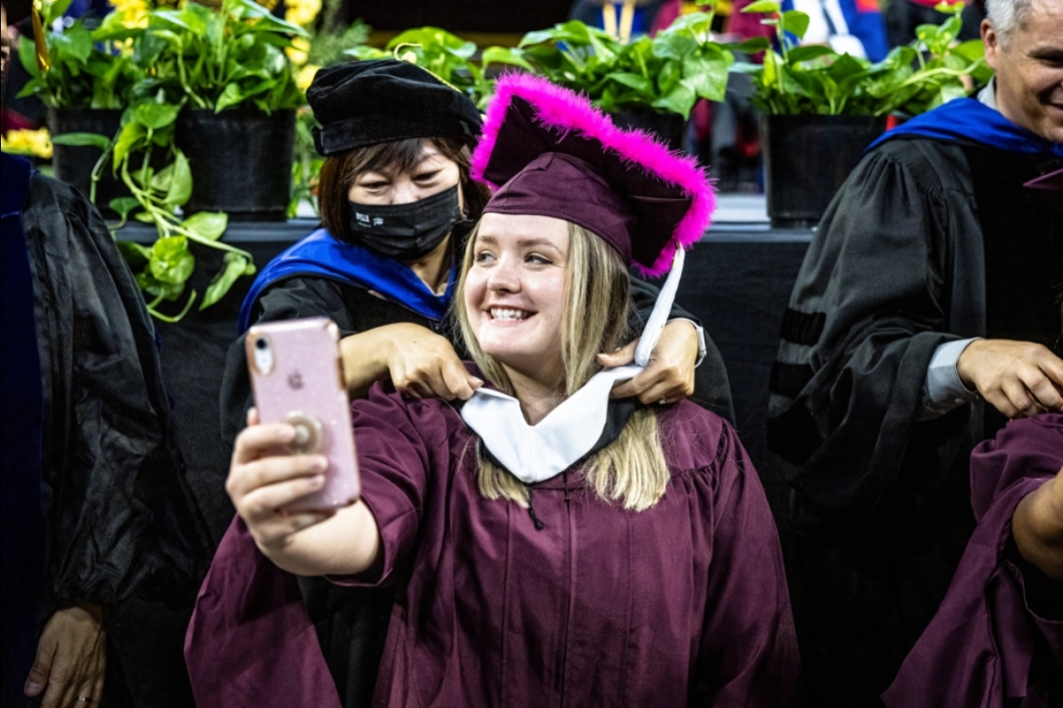 woman taking a selfie as she receives her master's hood at Graduate Commencement