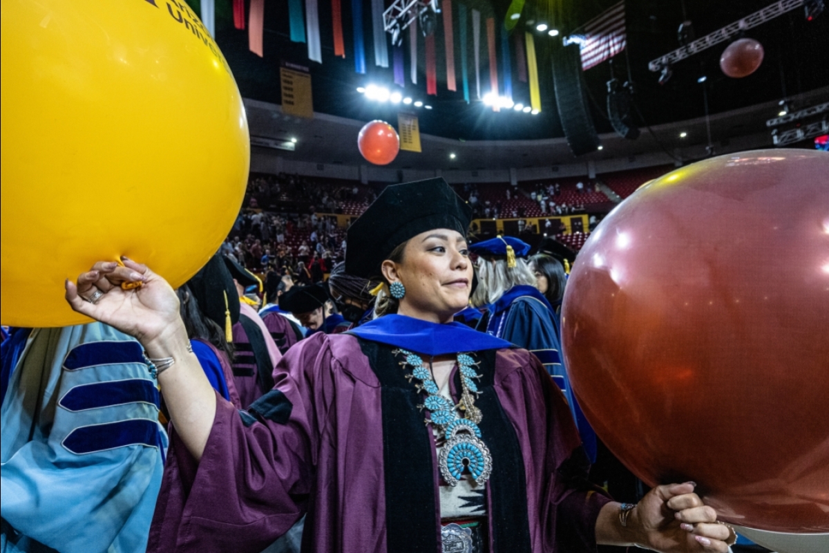 Doctoral student holding maroon and gold balloons during commencement.