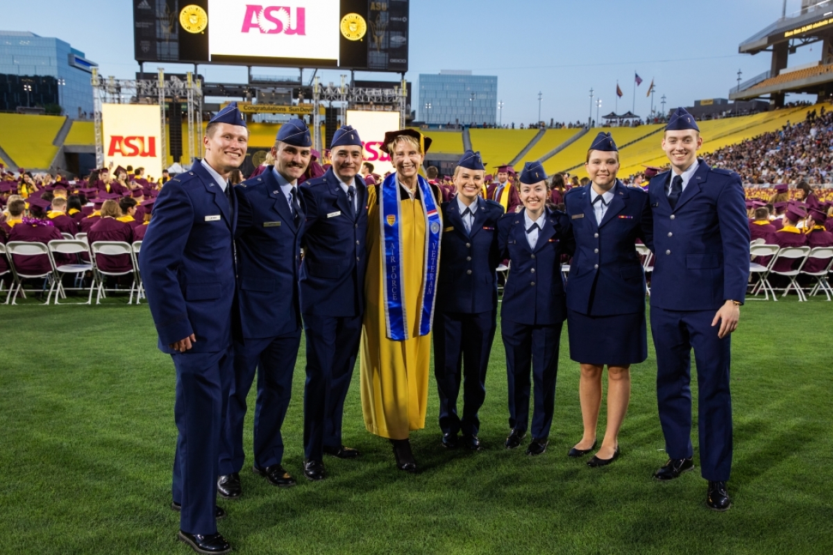 An older woman in a golden graduation gown poses for a group photo with seven Air Force ROTC members