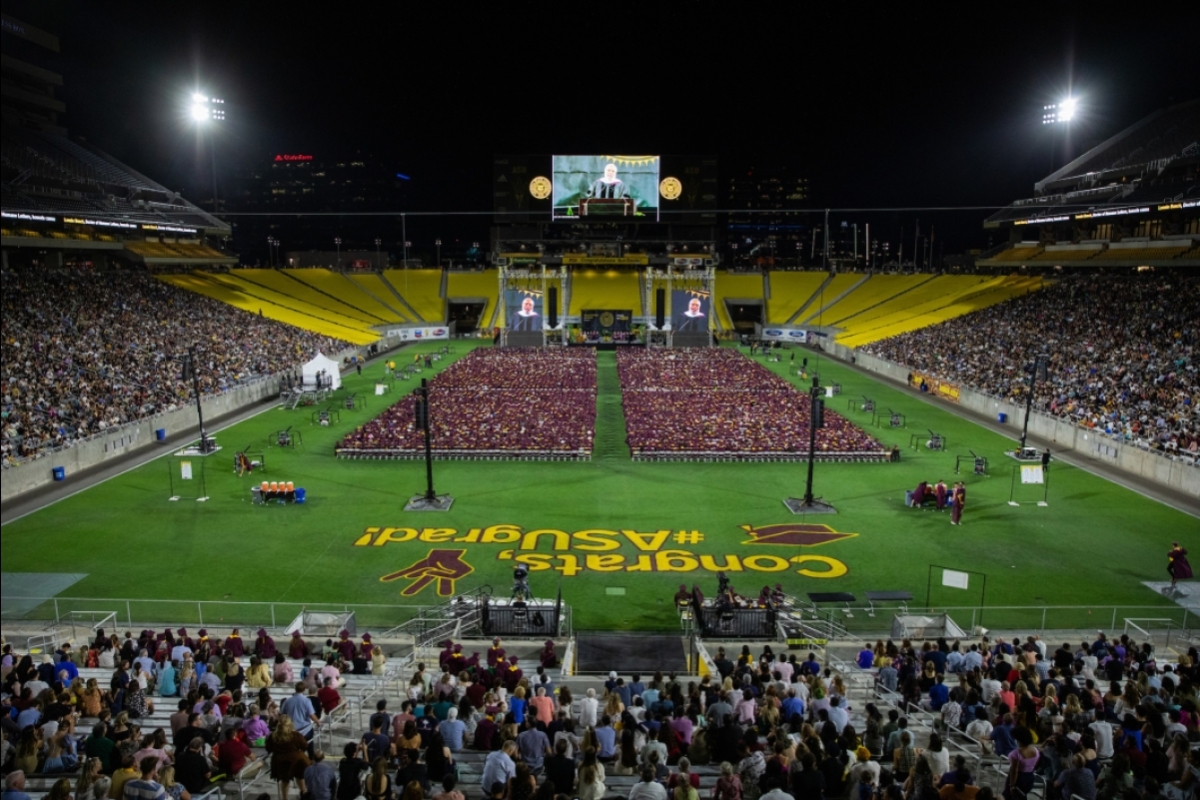 A wide shot of a football stadium with graduates filling the field