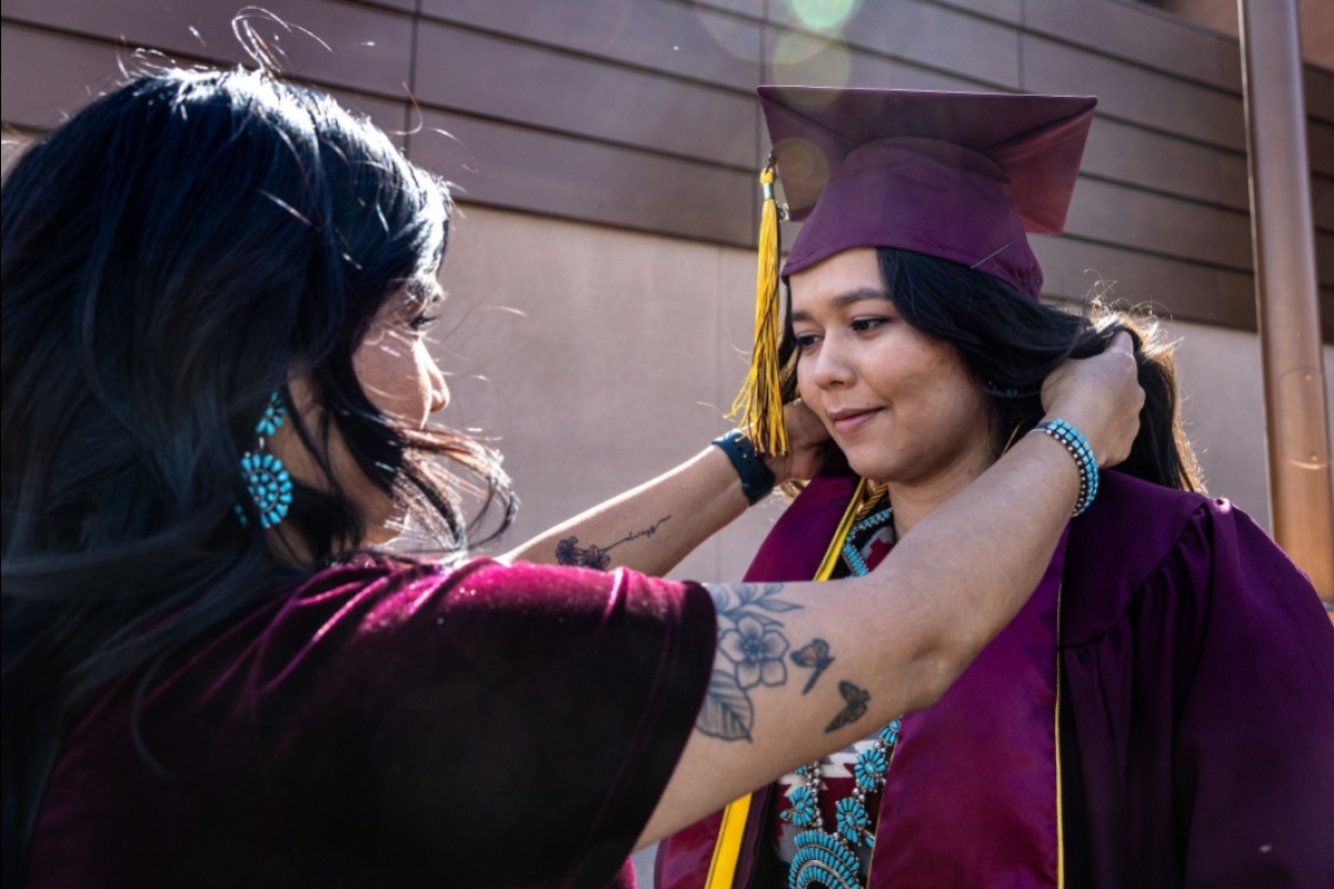 A woman in cap and gown gets help with her stoles from a woman facing her