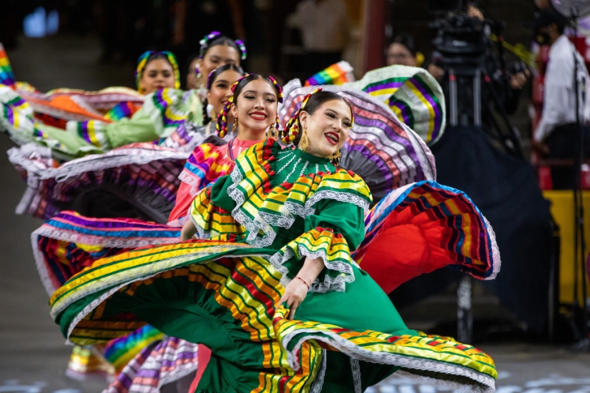 Hispanic dancers in colorful outfits perform in aisle at convocation