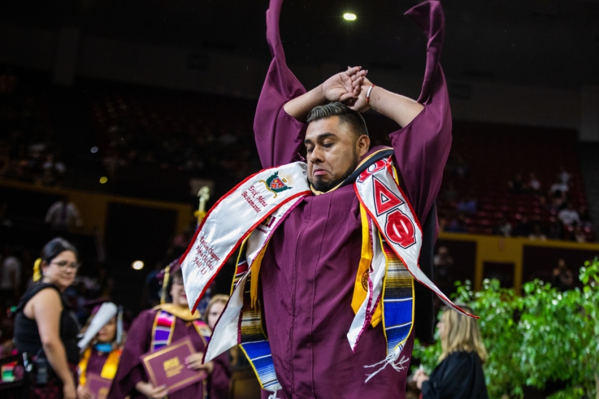 Graduate dancing across the stage with his arms raised
