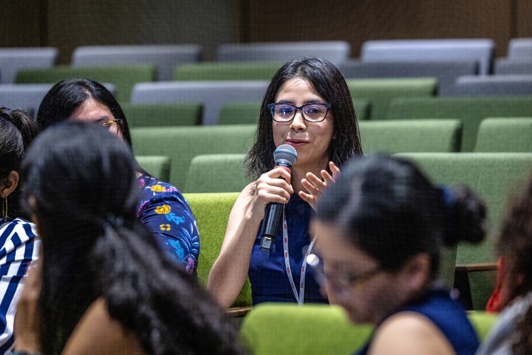 Woman seated in an auditorium speaking into a microphone.