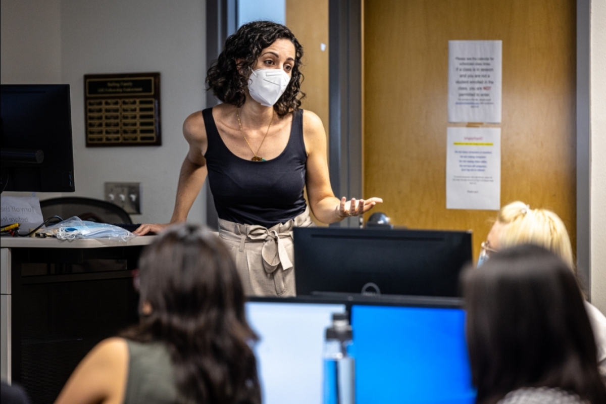 Woman wearing a face mask speaking to people in a classroom.