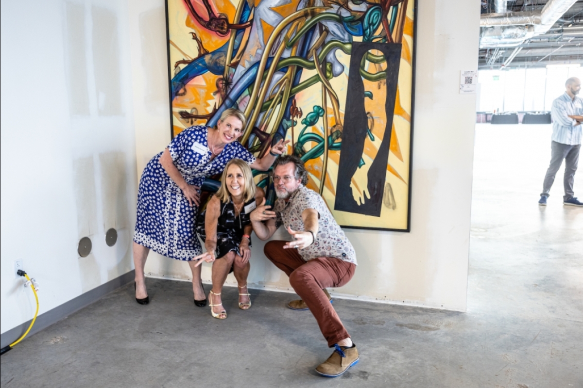 Three people pose in front of an abstract painting in a gallery space.