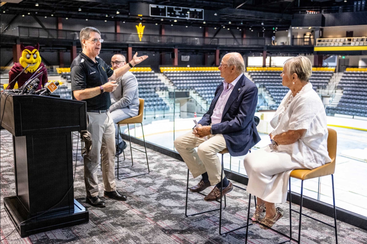 Man talking to two people sitting in chairs inside hockey arena for event
