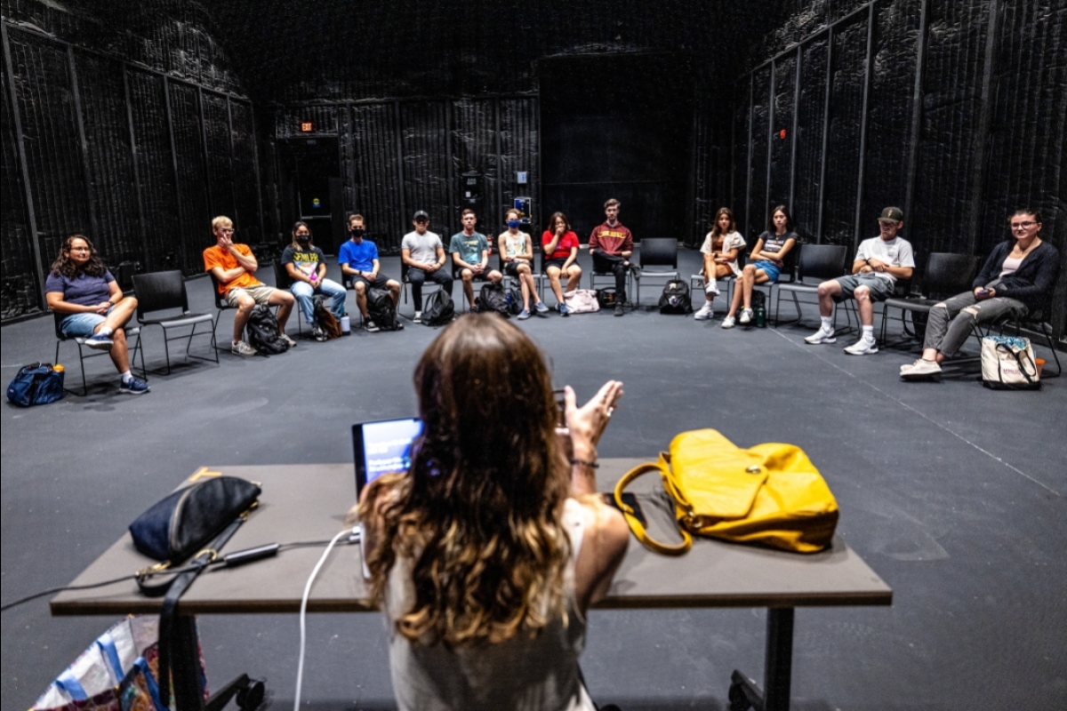 Professor at a table and students sitting in a semi-circle on a large sound stage