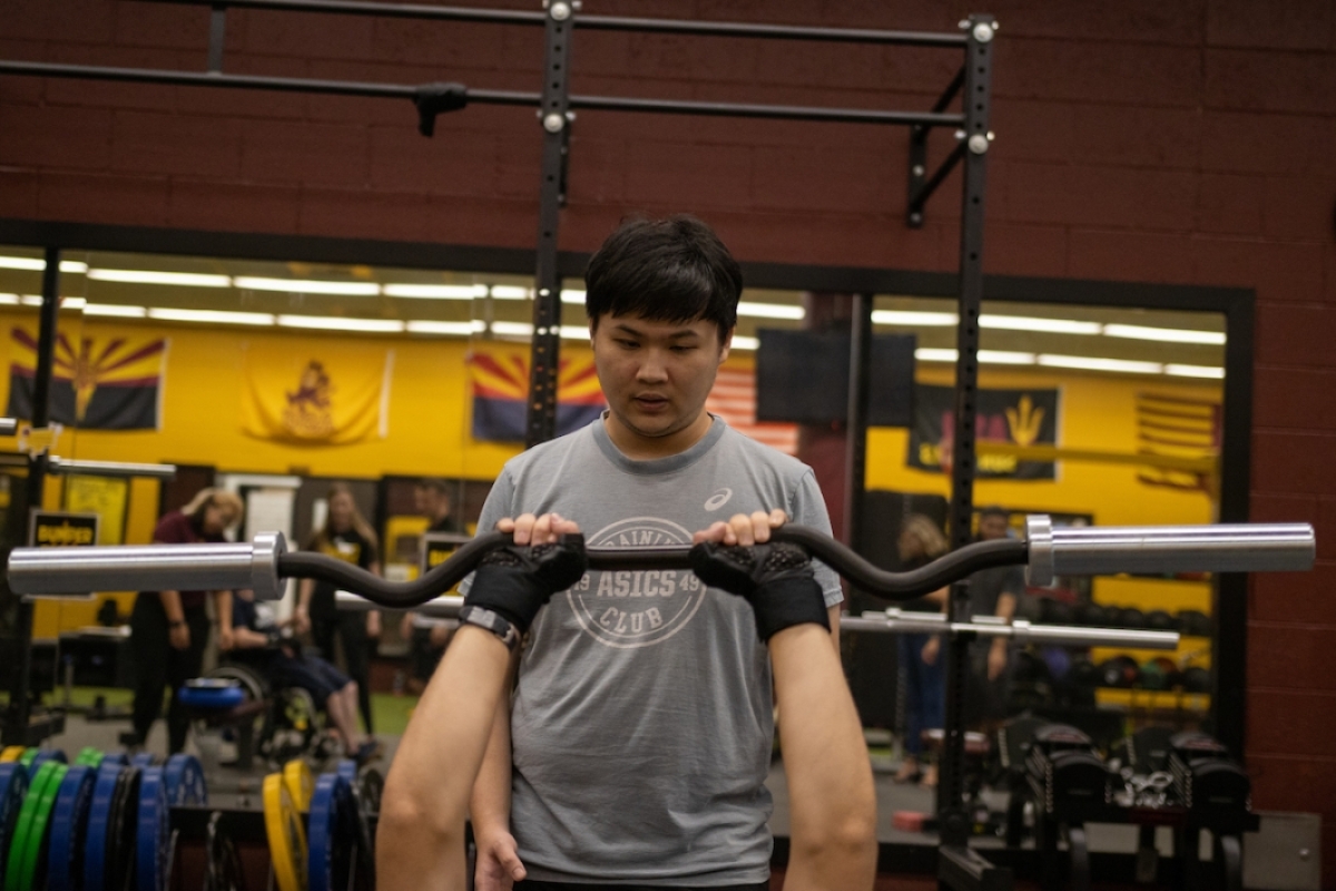 Student standing behind another student as he raises a barbell while lying on a weight bench.