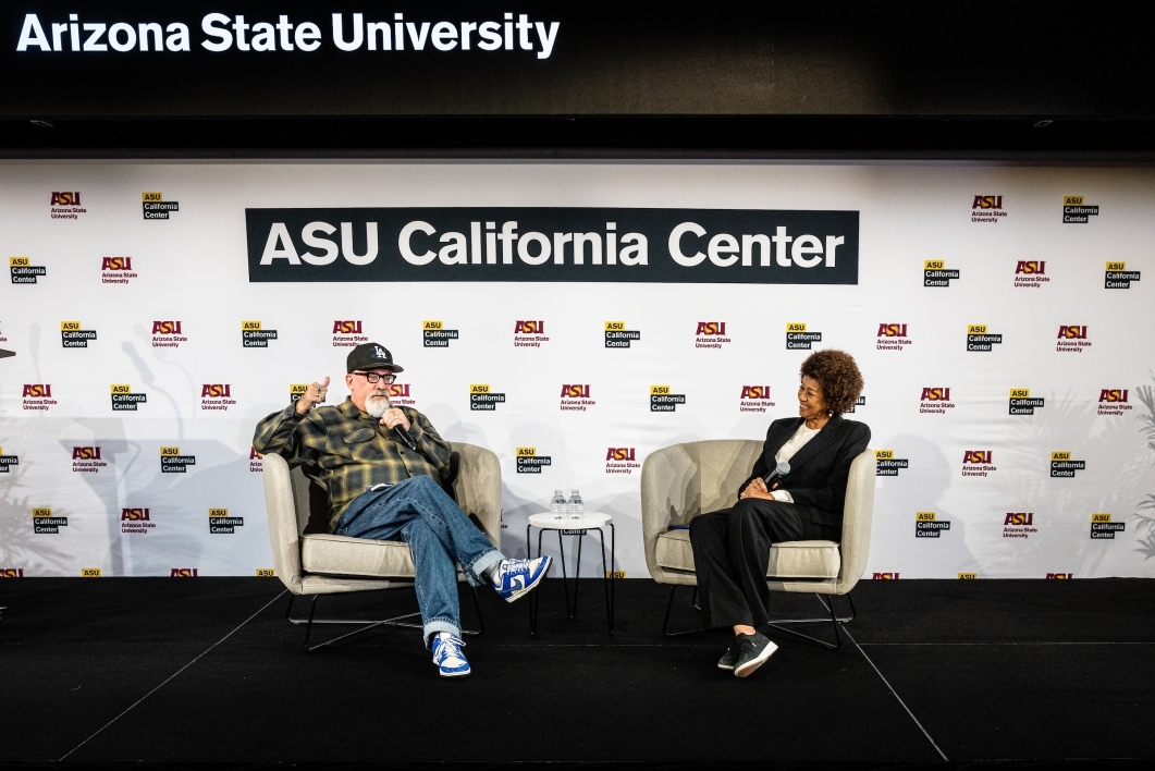 Two people sitting on stage in front of ASU backdrop, talking during event