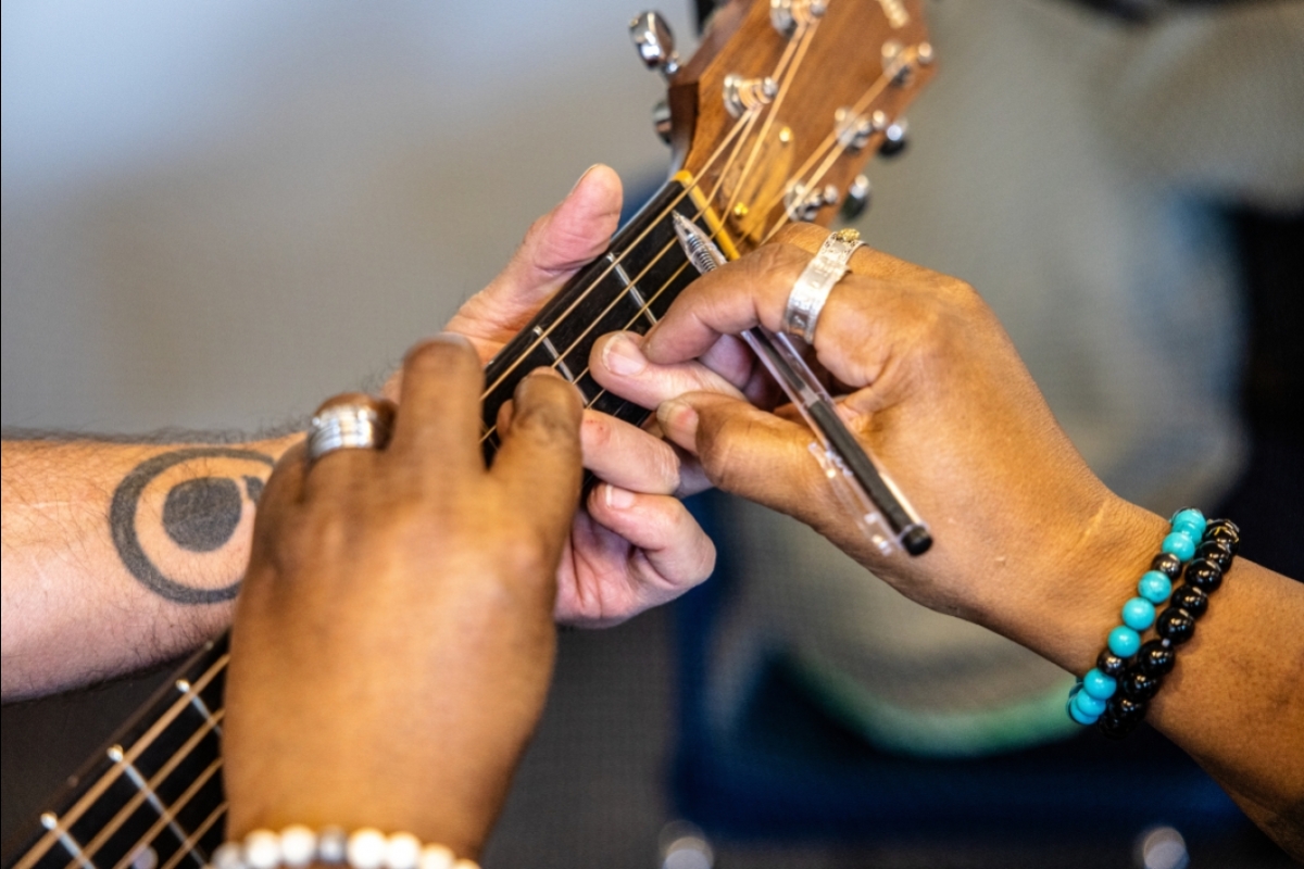 Person adjusting another person's finger position on a guitar neck