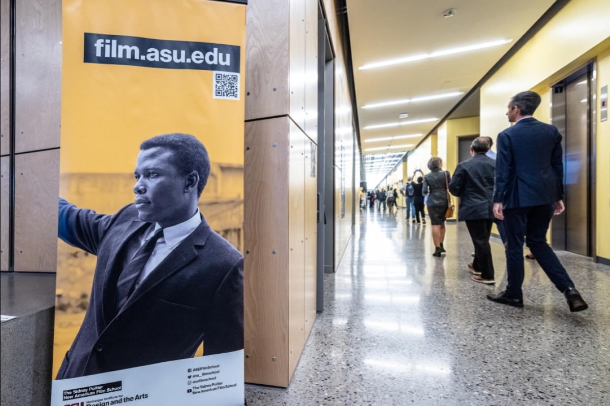 People walk down hallway of building next to a sign of Sidney Poitier