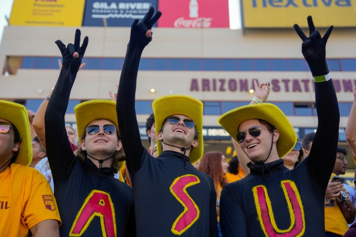 Three people wearing shirts that spell ASU holding up pitchfork signs