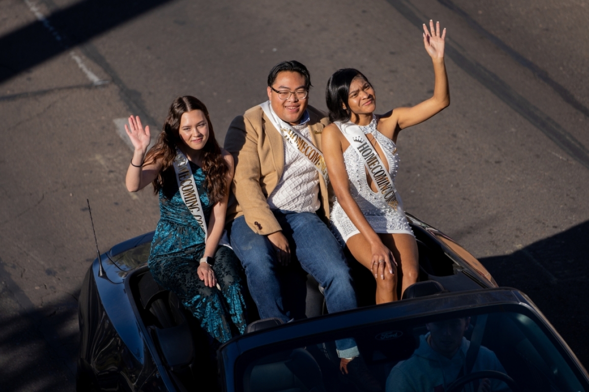 Three people riding in open car in parade