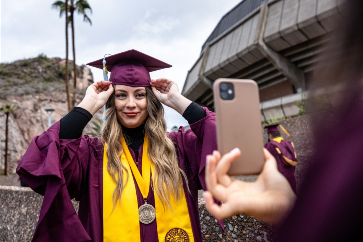 An ASU grad adjusts her cap while getting her photo taken