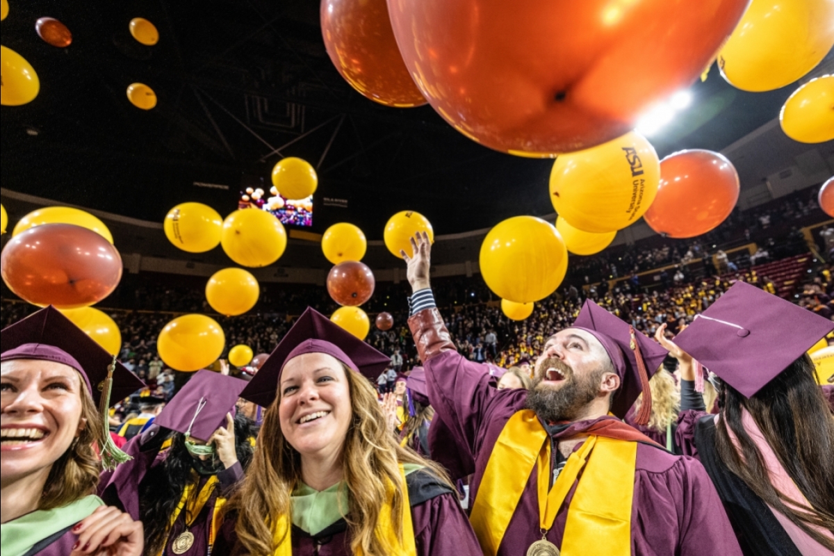 Students reaching up toward balloons at end of graduation ceremony