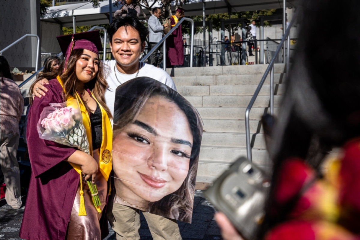 Graduate and friend posing with large photo of graduate at commencement