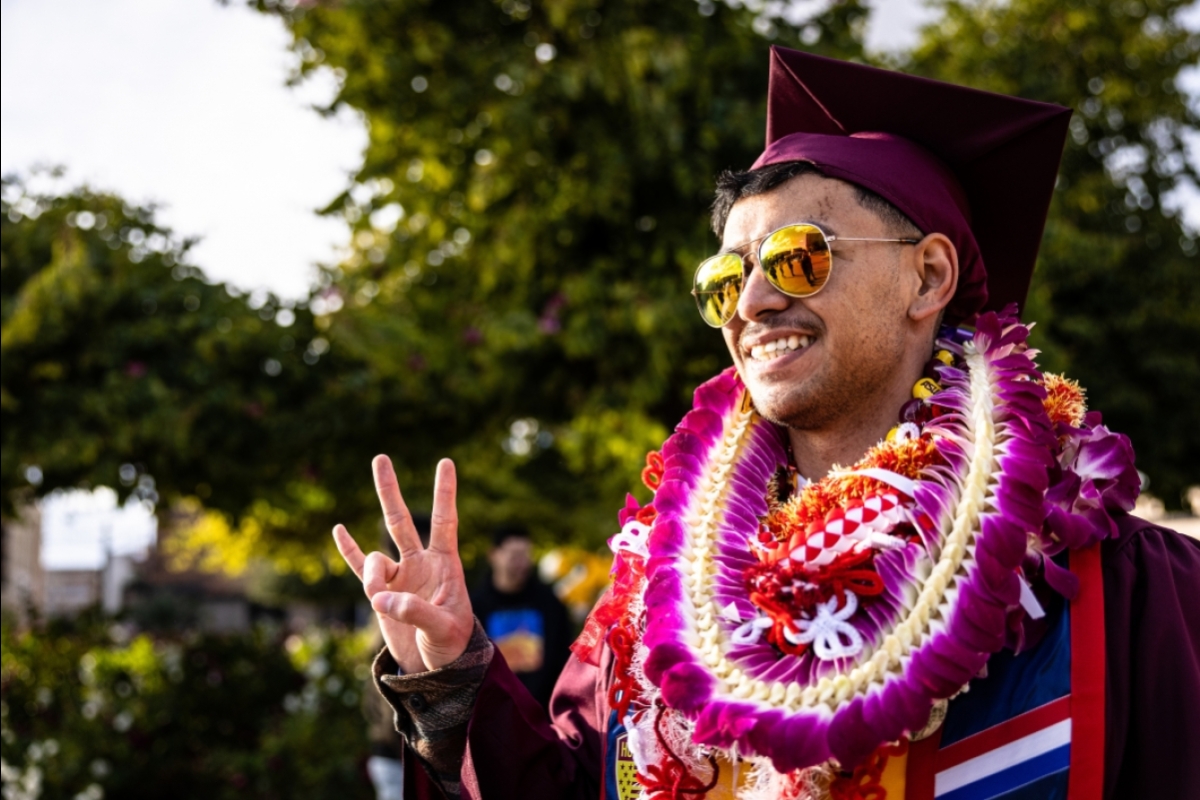 Graduate wearing sunglasses and leis flashes pitchfork sign