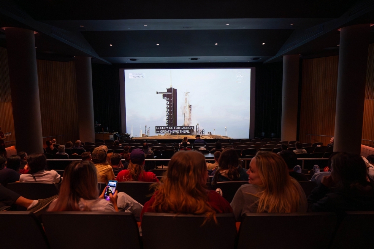 A crowd in a theater watches the Psyche launch livestream on the screen