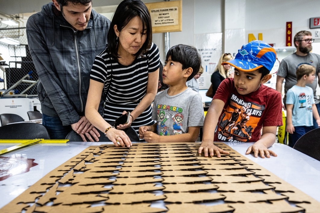Two adults and two children observe a laser-cut wood piece.