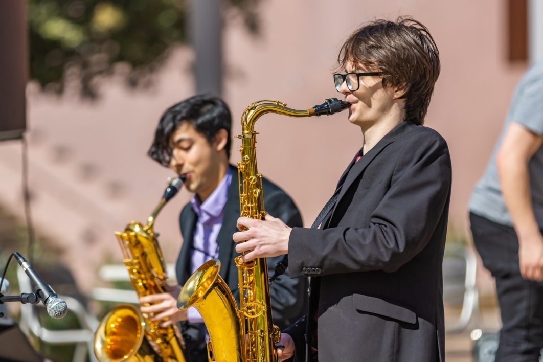 Two men playing saxophones on stage during outdoor event