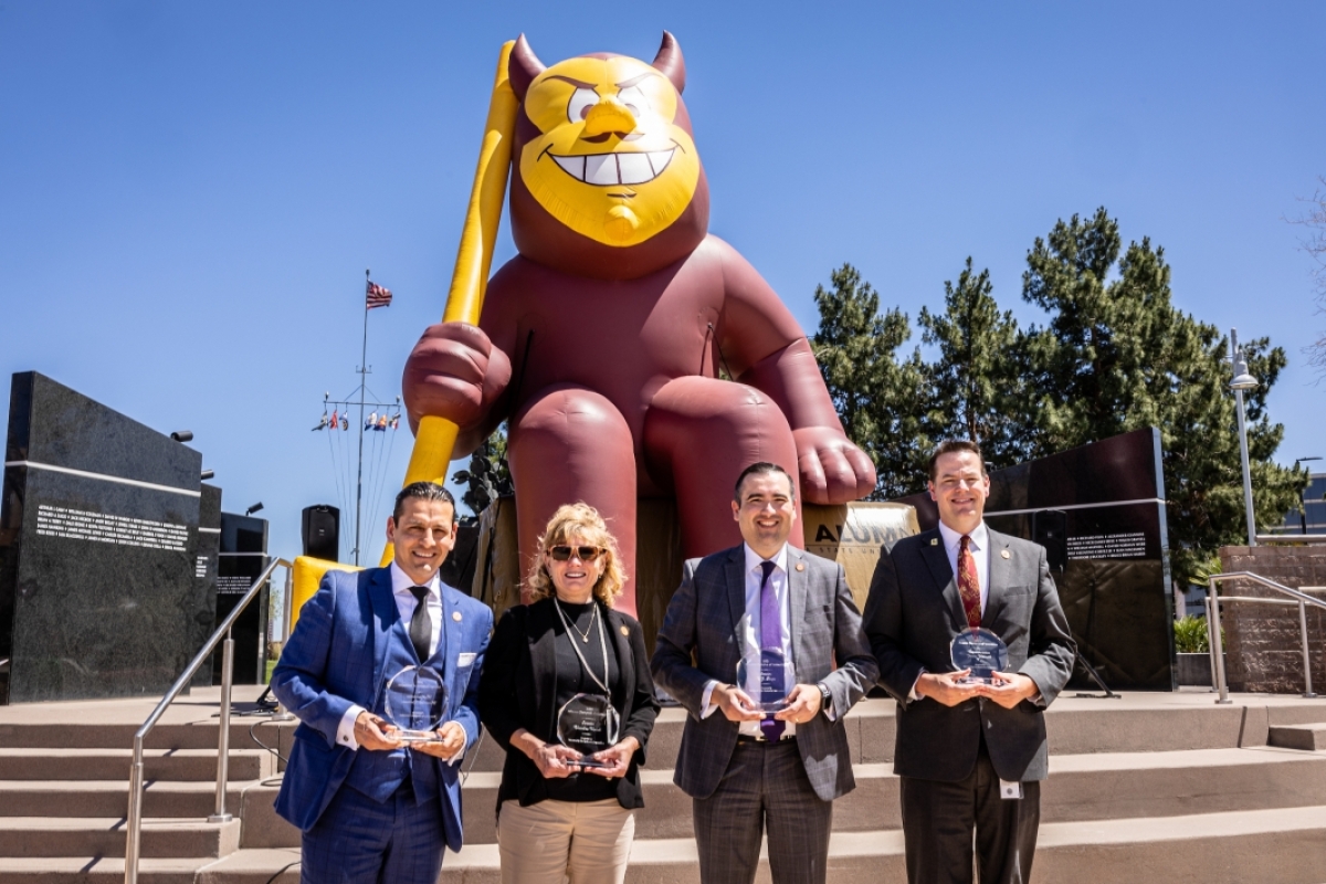 Four people holding awards standing in front of a giant inflatable Sparky mascot